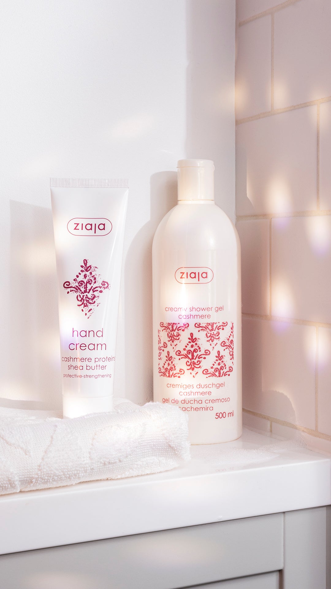 Ziaja Cashmere hand cream tube and Cashmere creamy shower gel (500 ml) on a bathroom counter with a folded white towel and tiled wall.