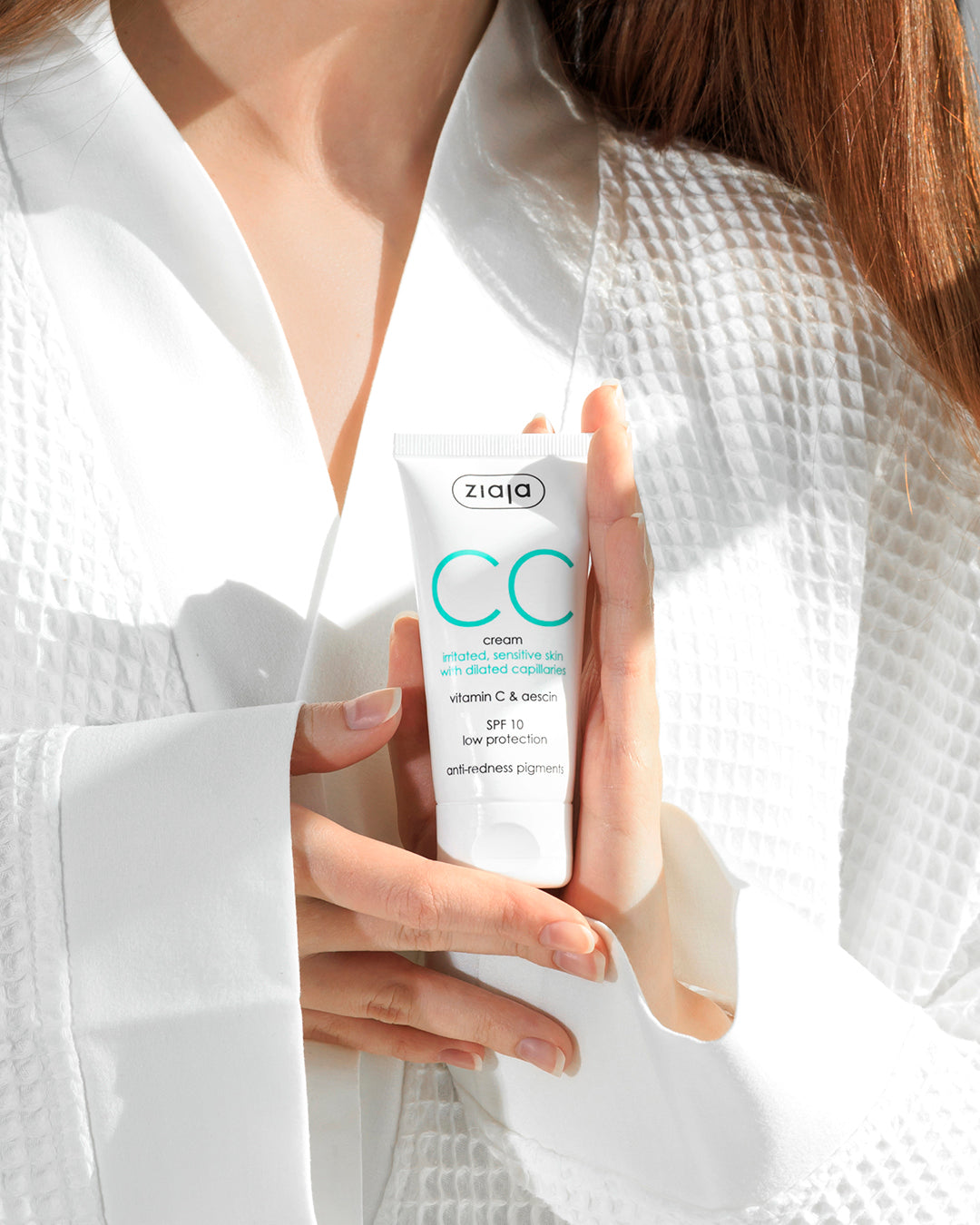 Person holding a Ziaja CC cream with a white robe in the background