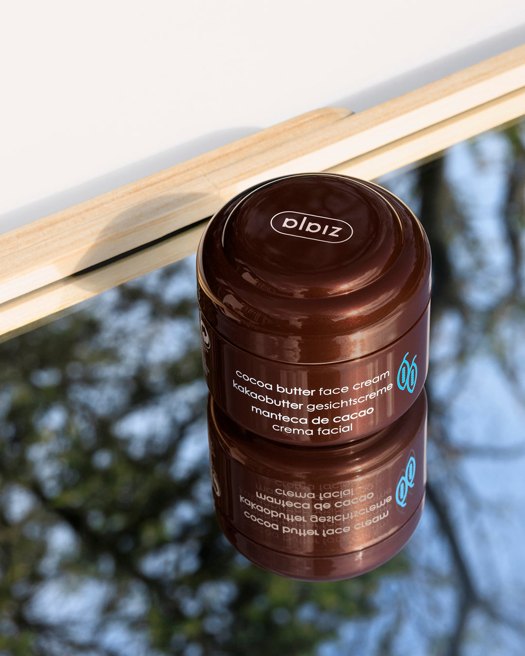Brown jar of cocoa butter face cream with visible brand name on a blurred natural background