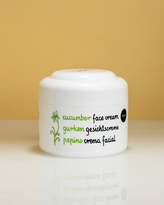 A white cosmetic jar cucumber face cream, featuring green and black text and a small green leaf illustration, set against a warm yellow background.