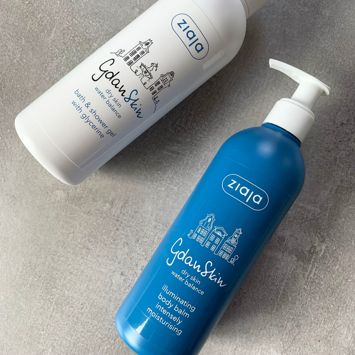Two Ziaja Gdanskin skincare products on a gray surface, one blue bottle and one white bottle.