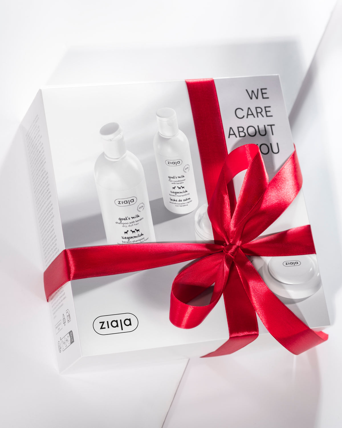 Ziaja Goat’s Milk hair care gift set with keratin shampoo, conditioner and hair mask, presented in a white “We Care About You” box tied with a red satin ribbon.