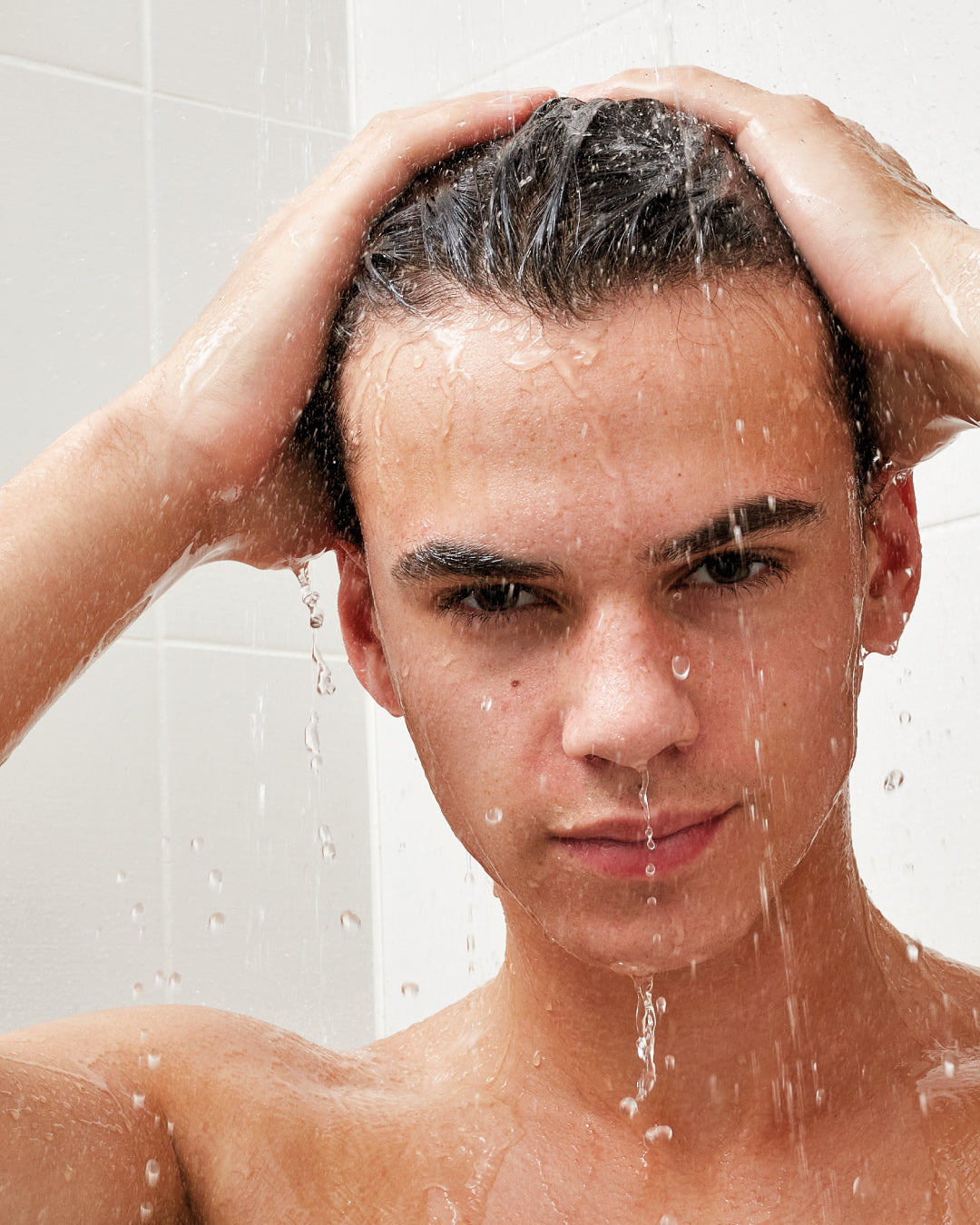 Person washing their hair under running water in a bathroom setting