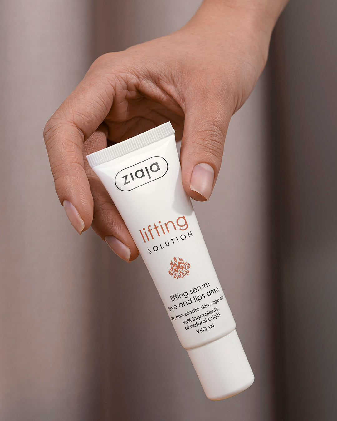Hand holding a Ziaja lifting solution cream tube against a neutral background