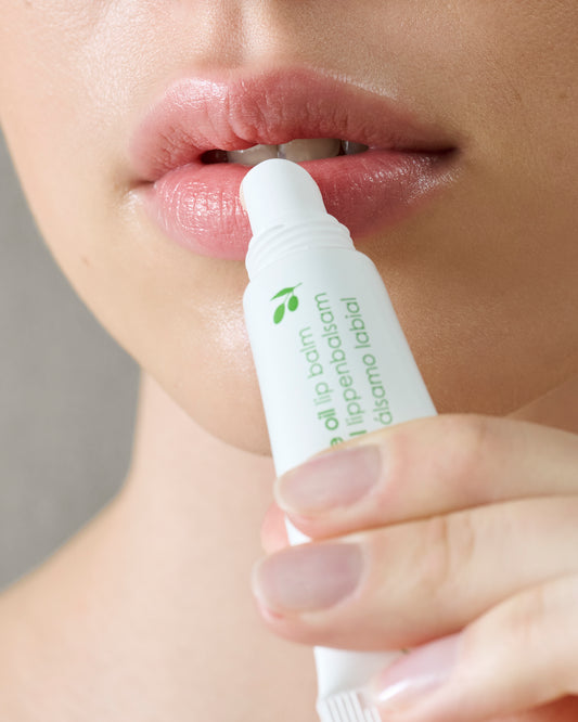 Person applying Ziaja olive oil lip balm to their lips with a focus on the product.