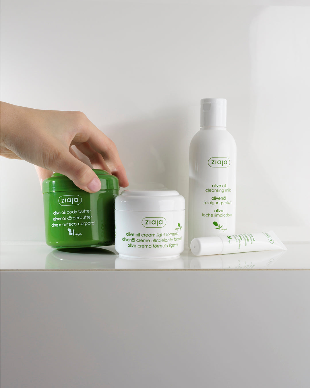 Ziaja skincare products on a white surface with a hand reaching for a jar.