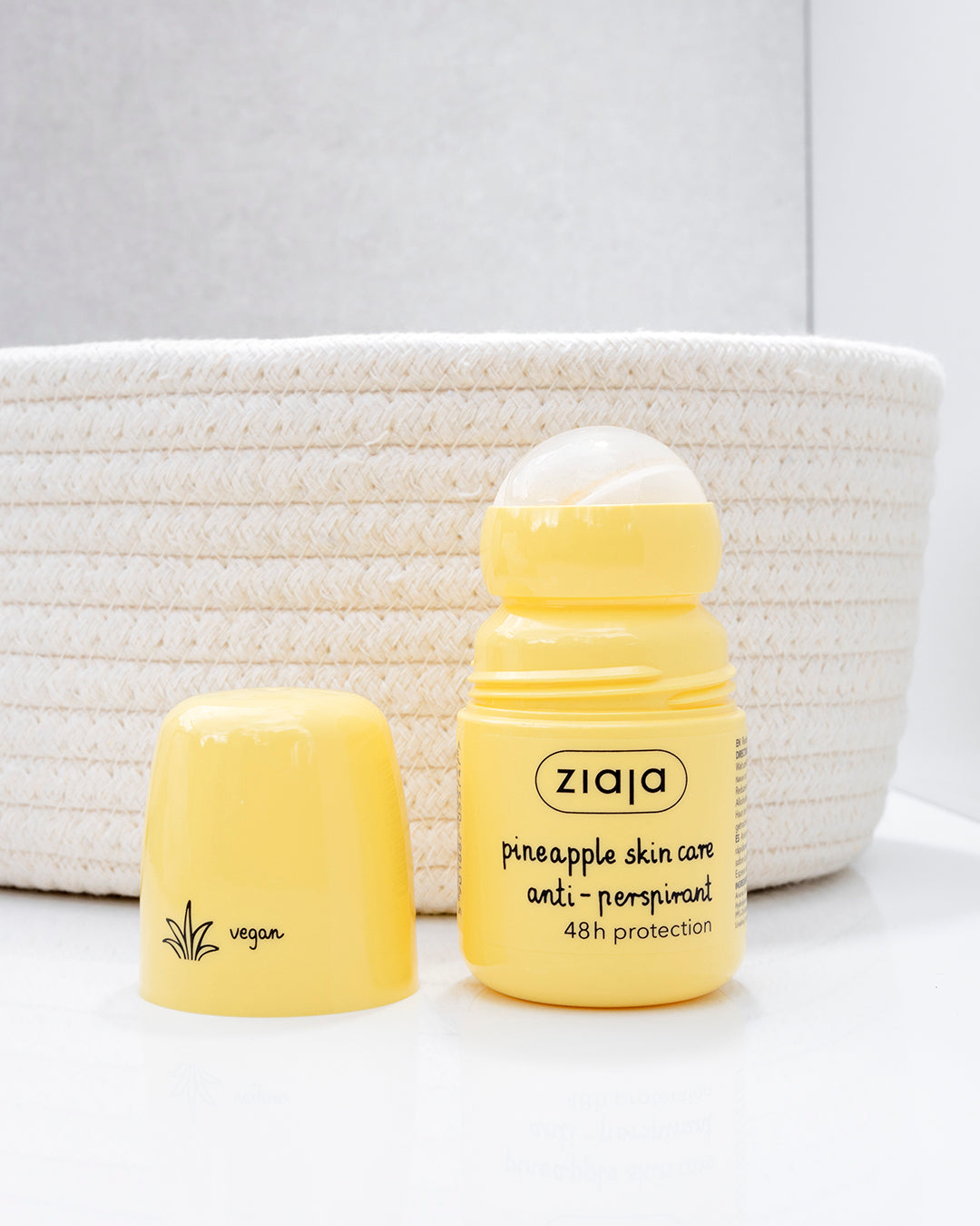 Ziaja Pineapple Skin Care anti-perspirant roll-on (48h protection) in a yellow bottle with the cap placed beside it, photographed on a white surface in front of a woven basket background.