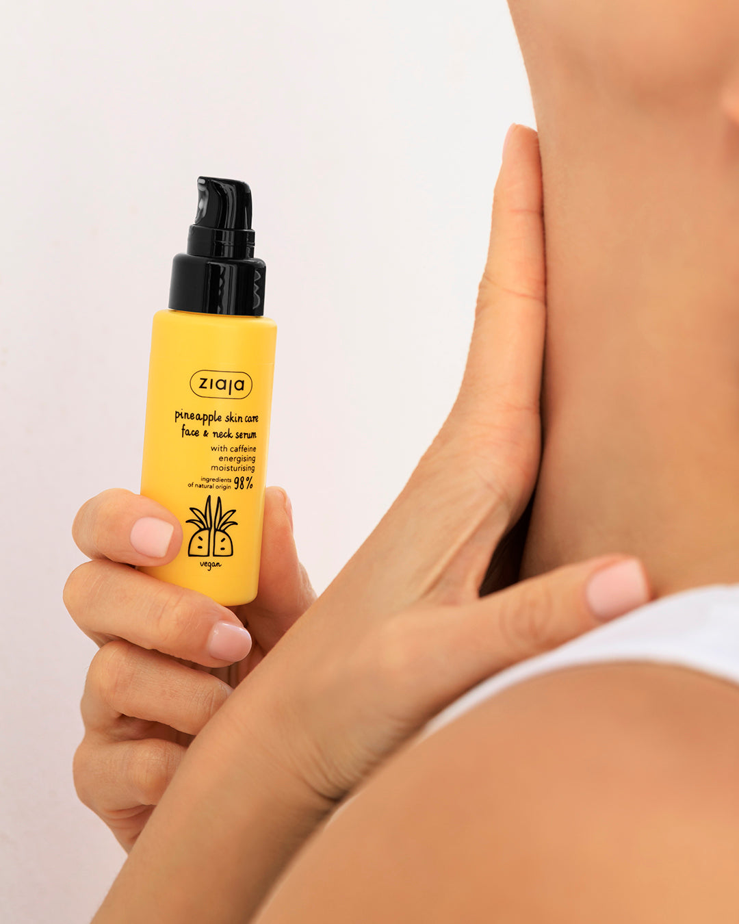 A person holding a yellow bottle of Ziaja Pineapple Skin Serum against a clean white background.
