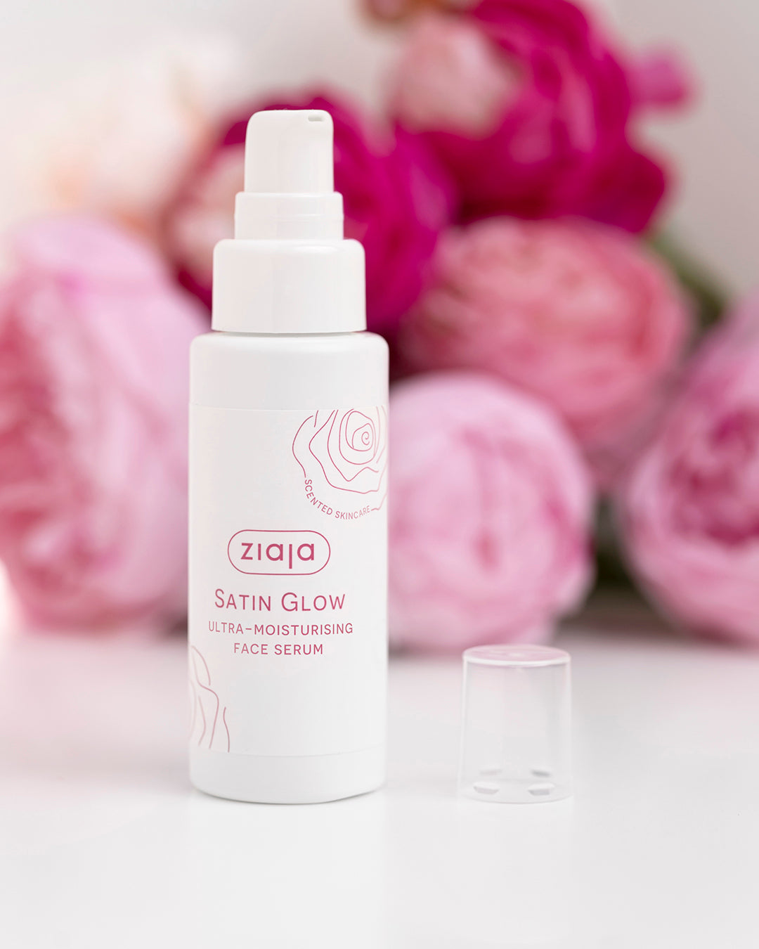 Ziaja Satin Glow face serum bottle with pink flowers in the background