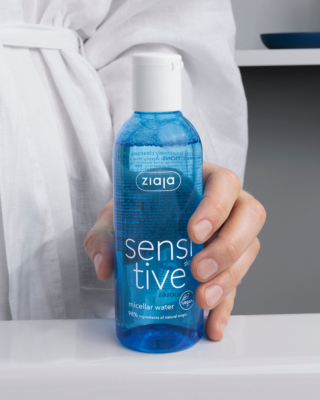 Person holding a blue bottle of Ziaja sensitive micellar water in a bathroom setting.
