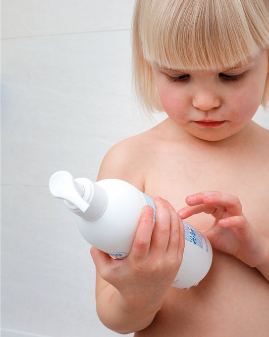 Toddler holding and looking at a bottle of Ziaja Baby body & hair shower gel in the bathroom.