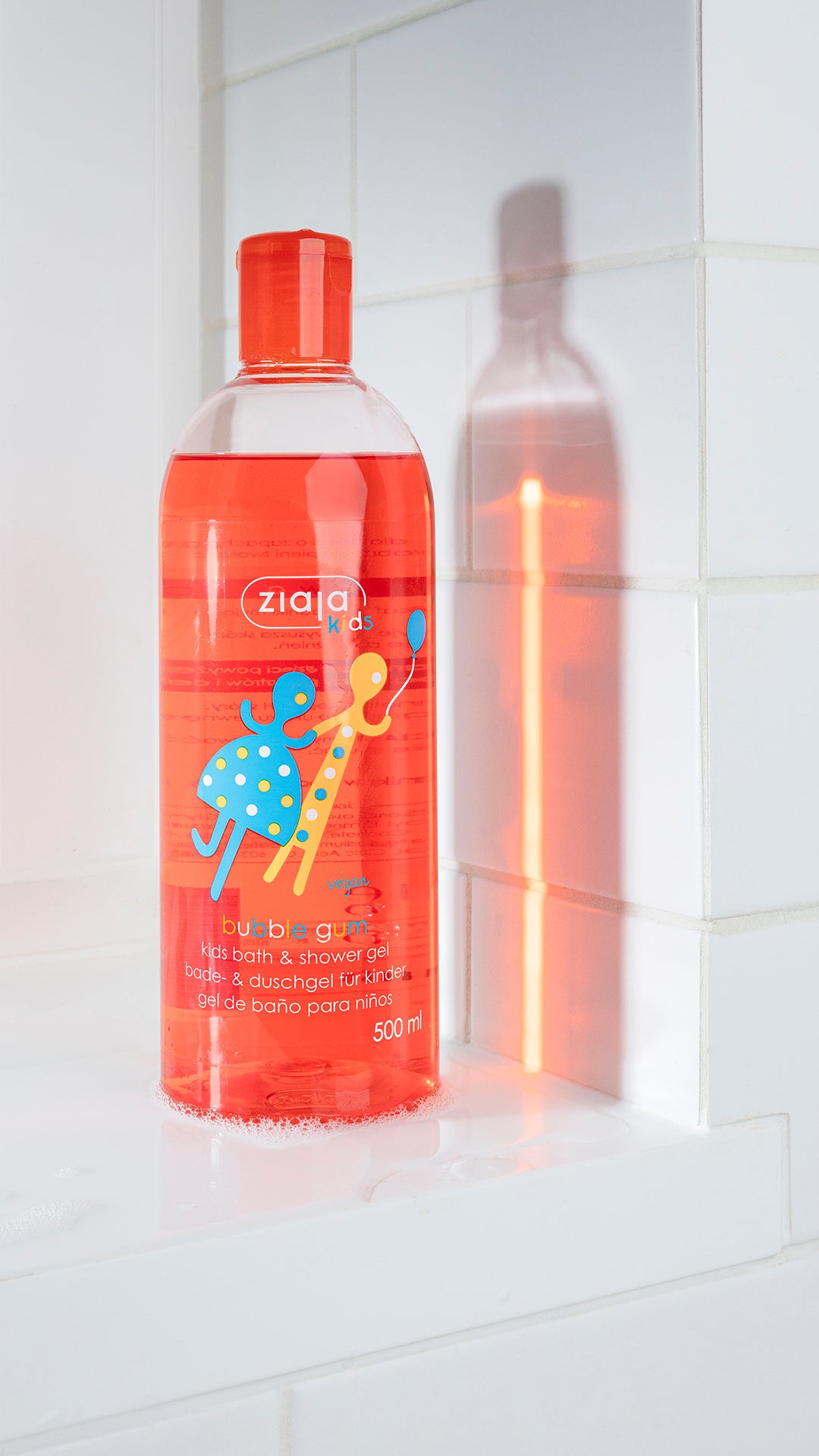 Red bottle of Ziaja baby shower gel on a white tiled bathroom shelf