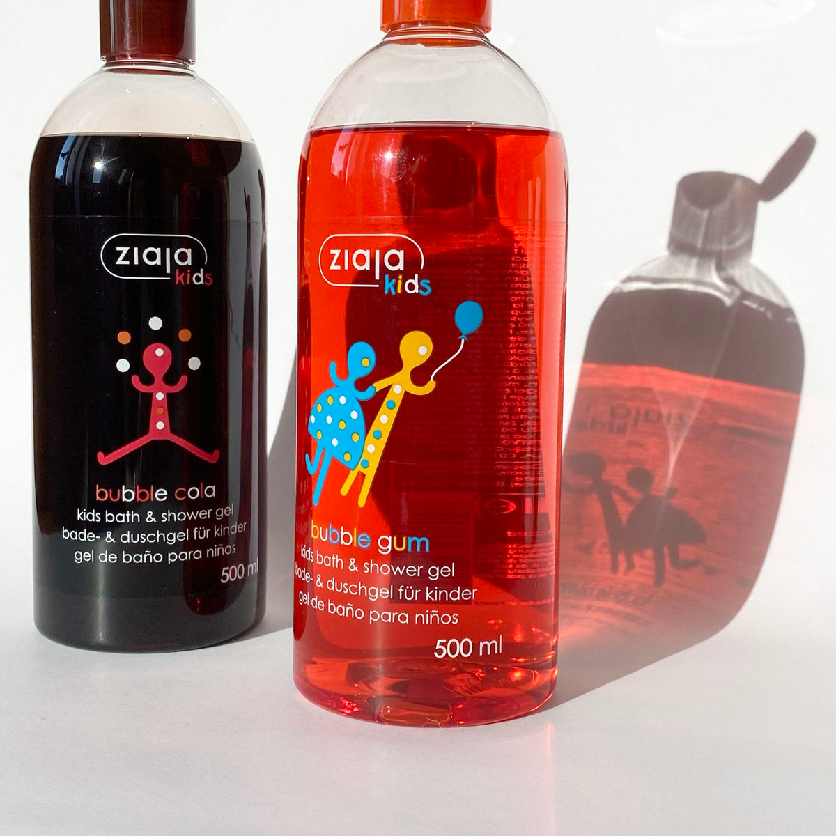 Two bottles of Ziaja Kids Bubble Gum kid bath & shower gel on a white background, one with dark purple gel and one with red gel, with a faded reflection of the black gel bottle on the right.
