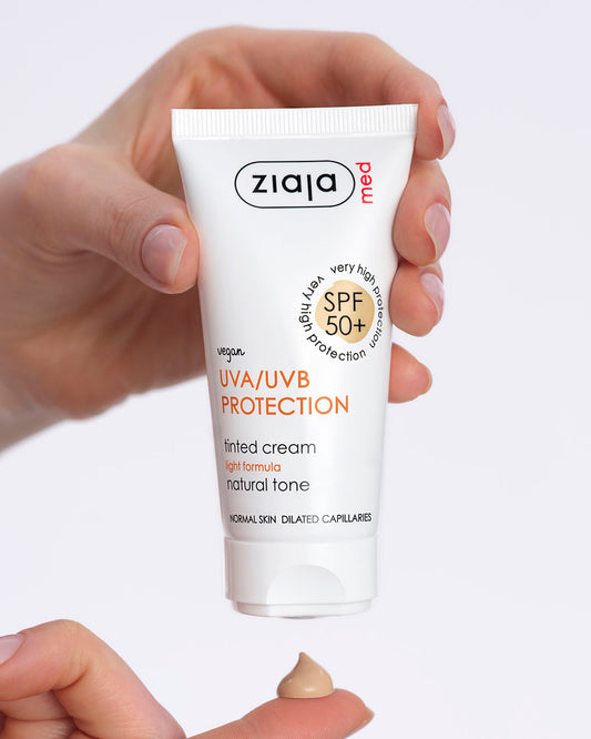 A hand holding a tube of Ziaja Med UVA/UVB Protection SPF 50+ tinted face cream against a light grey background, with a small dollop of the natural-tone cream on a fingertip below.