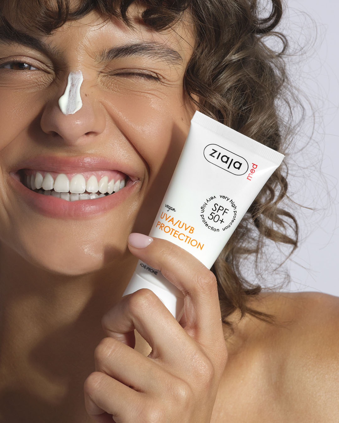 Woman applying Ziaja sunscreen cream to her face with a white background