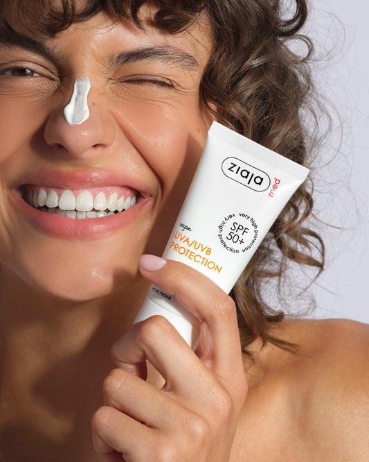 Woman applying Ziaja sunscreen cream to her face with a white background