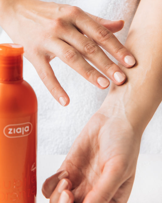 An orange bottle of Ziaja Subtle Bronze body lotion and hands applying the products to the inner forearm.
