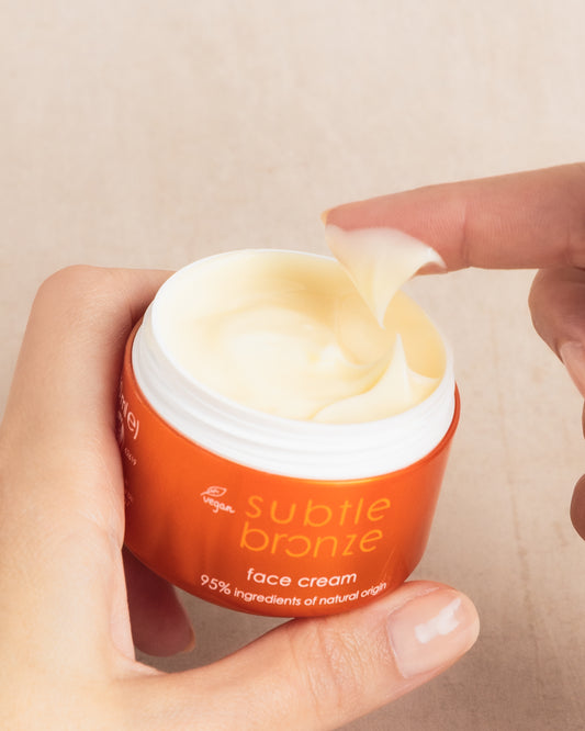 Hand holding a jar of 'subtle bronze' face cream with a beige background