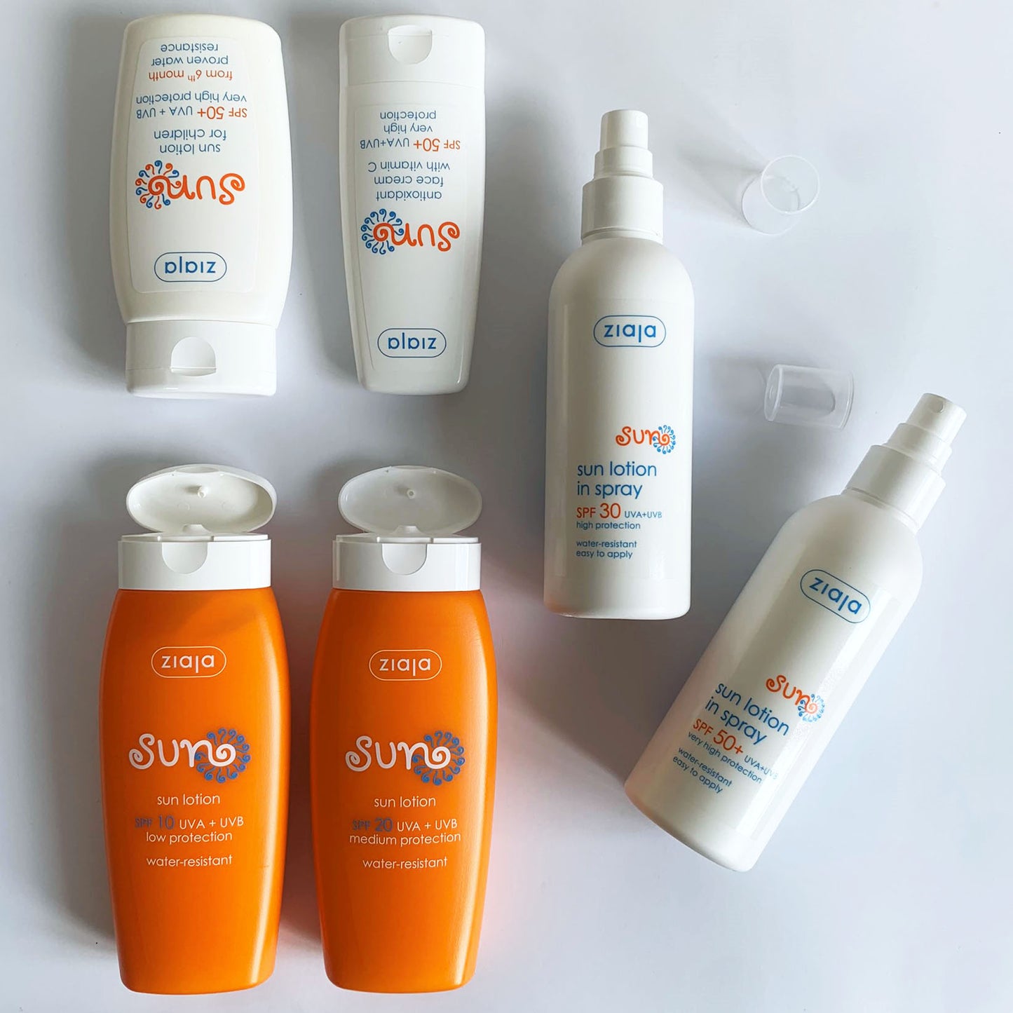 Ziaja Sun range flat lay on a white background – SPF 10 and SPF 20 sun lotions, children’s SPF 50+ lotion, SPF 30 spray lotion and SPF 50+ spray, with caps open