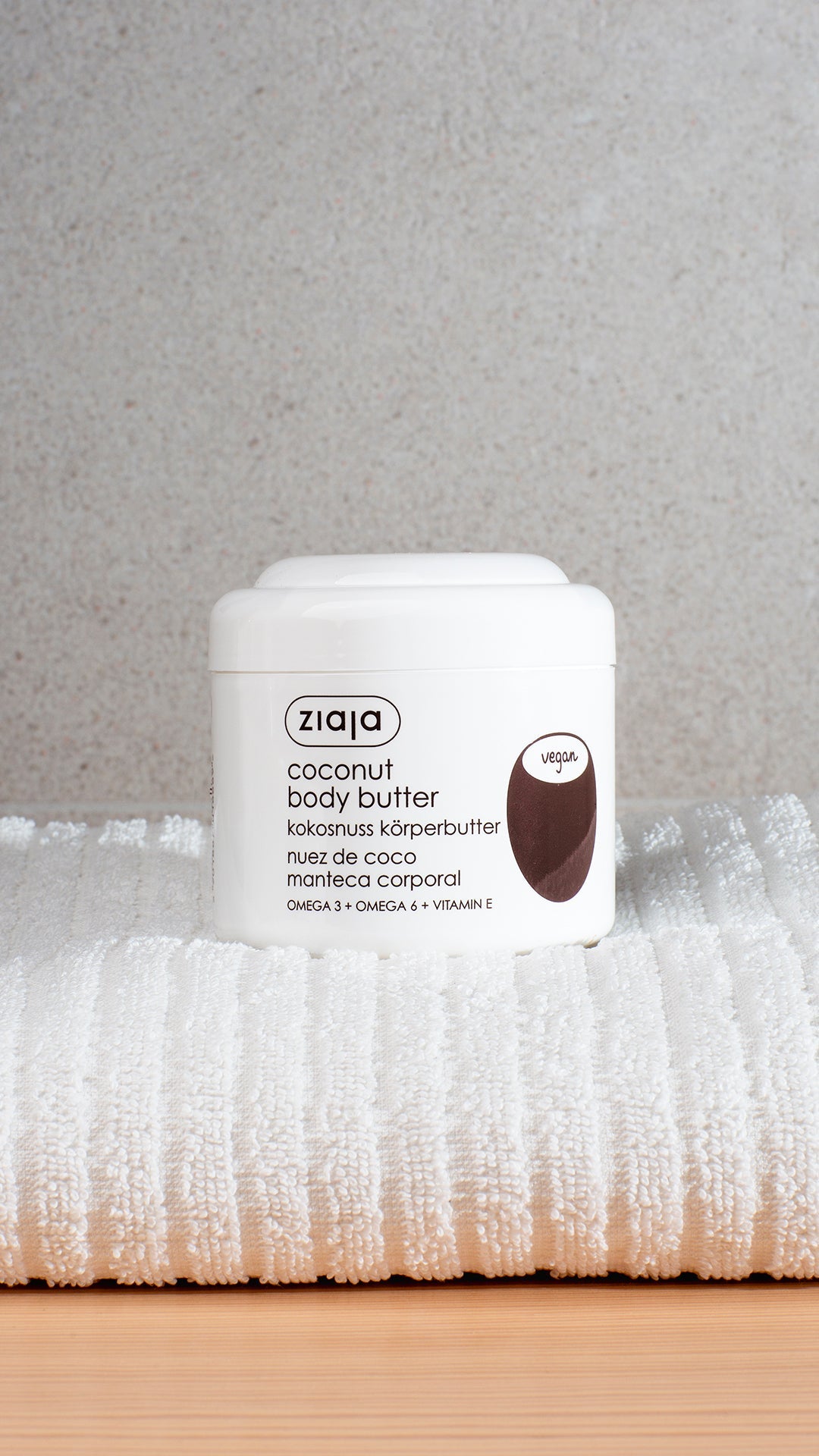 A white pot of Ziaja Coconut body butter placed ona. white towel. Brown letters and coconut image on the pot. 