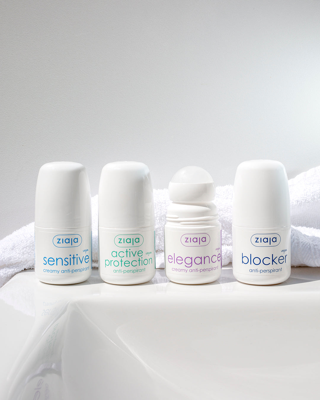 Four Ziaja roll-on anti-perspirants lined up on a bathroom surface with a towel behind: Sensitive, Active Protection, Elegance (open roll-on), and Blocker.