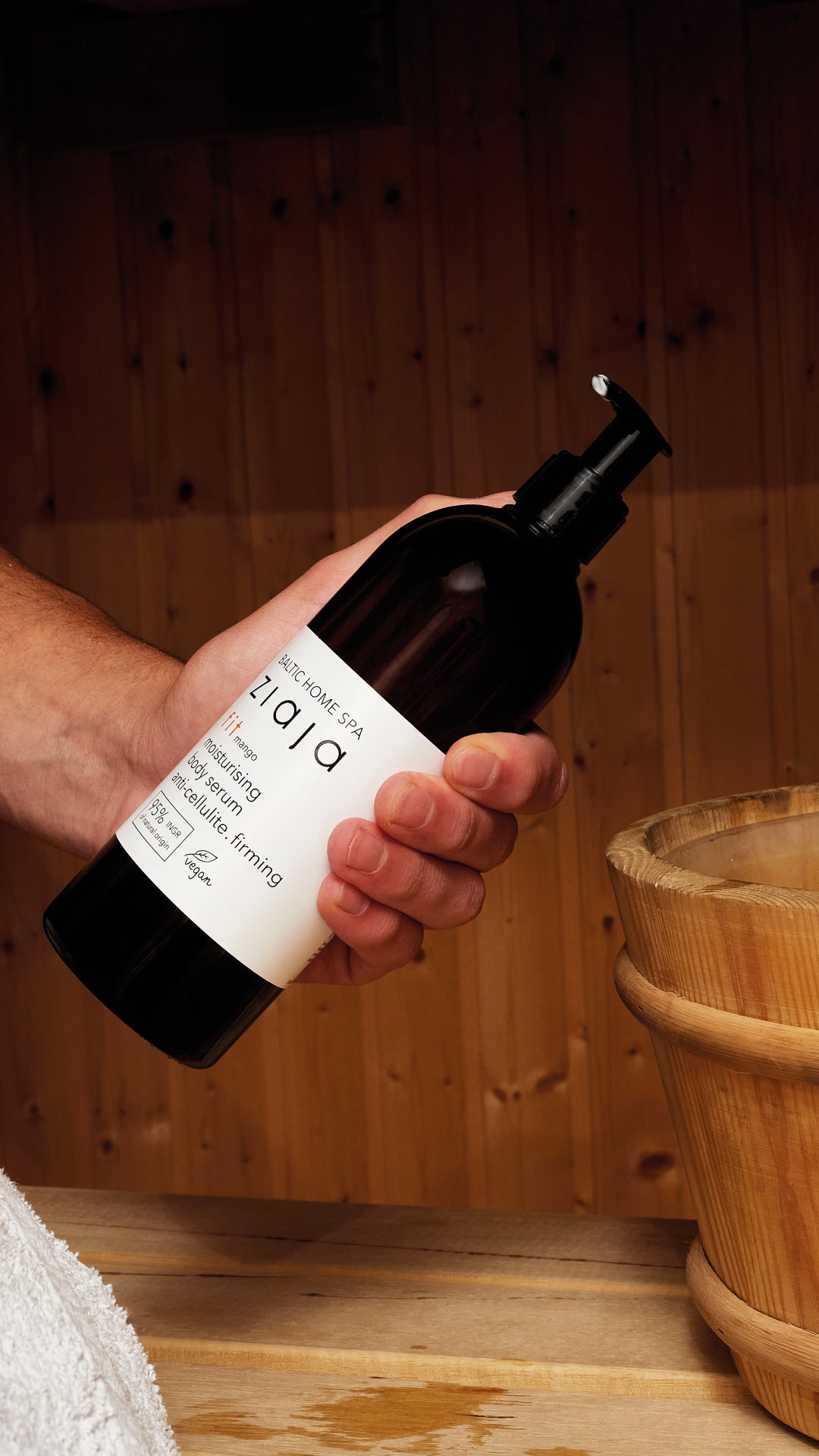Hand holding a bottle labeled 'Pajaj' in a wooden setting