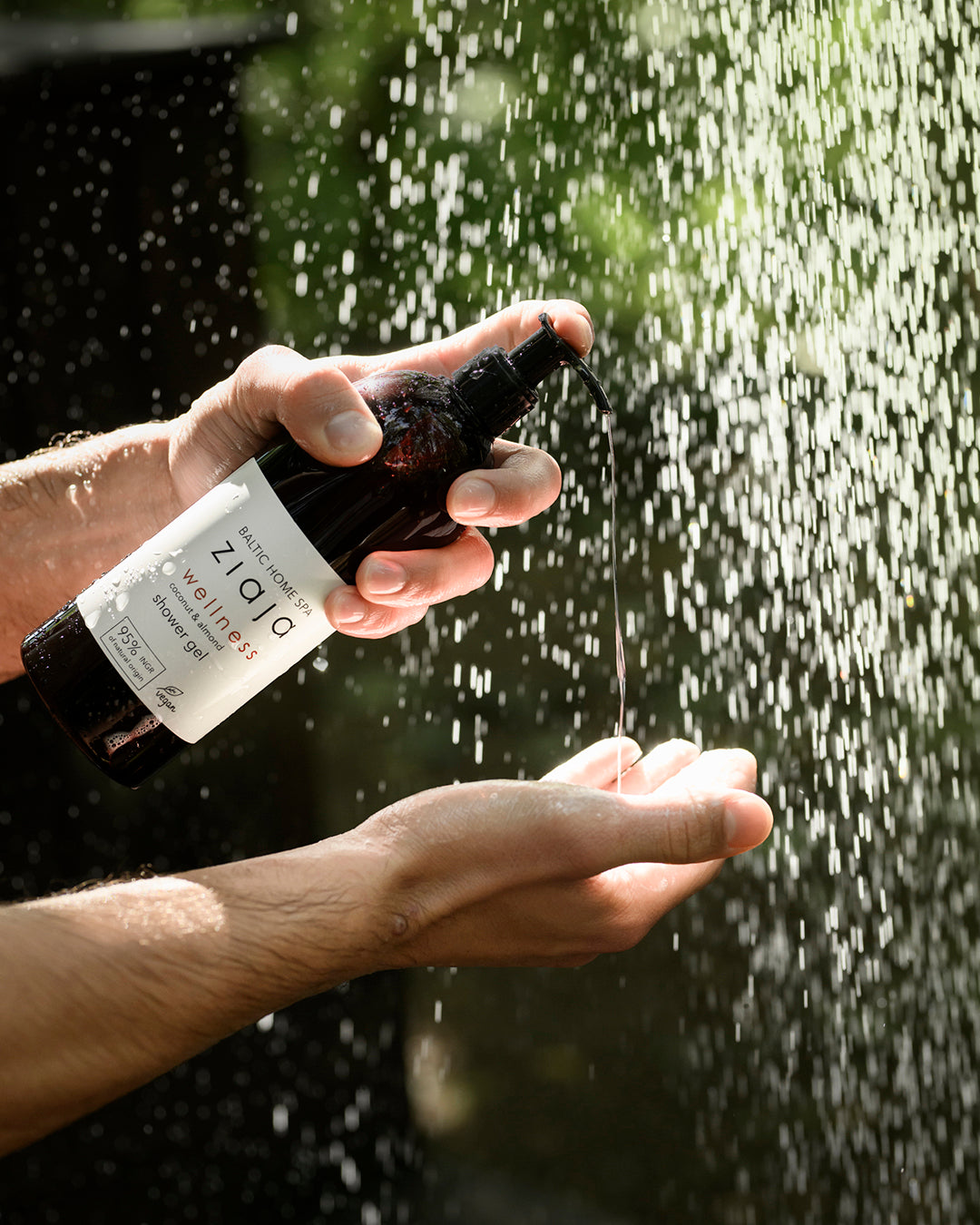 Person holding a bottle labeled 'Zilio' under a shower with water droplets visible.