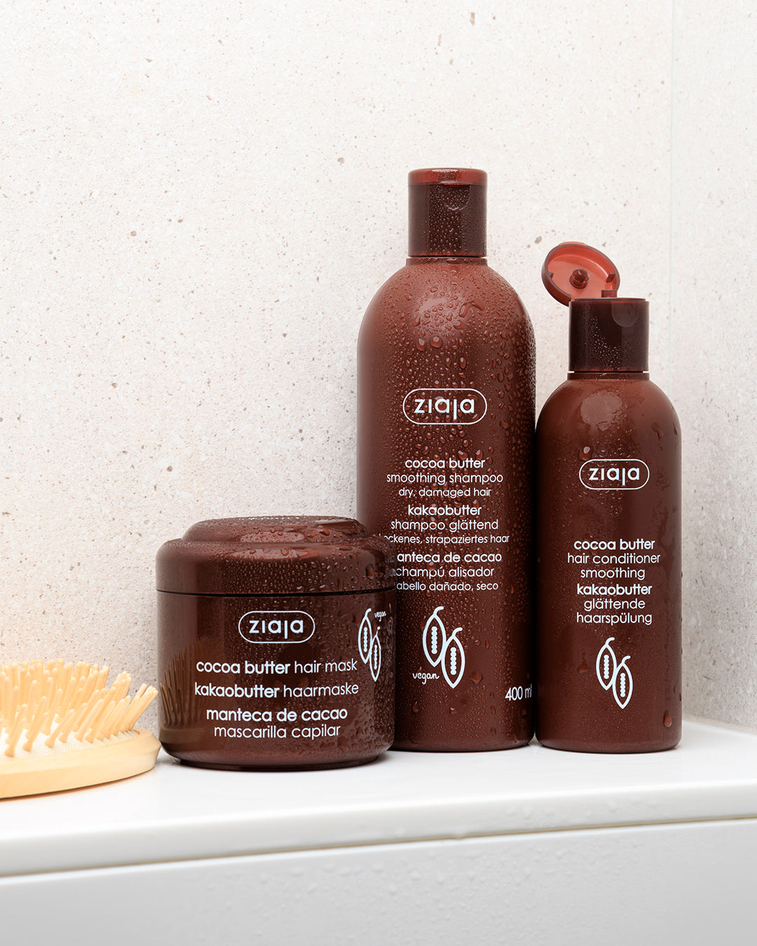 Ziaja cocoa butter shampoo, hair conditioner and hair mask in brown packaging placed on a white shelf