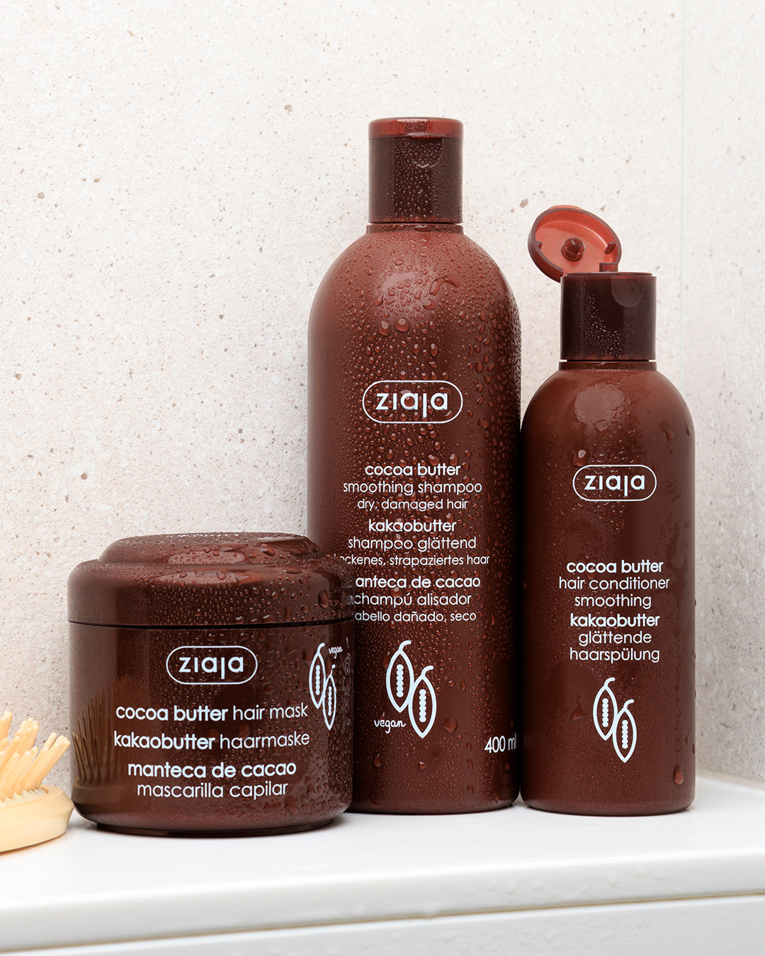 Ziaja cocoa butter hair care products on a white surface with a light gray textured wall background.