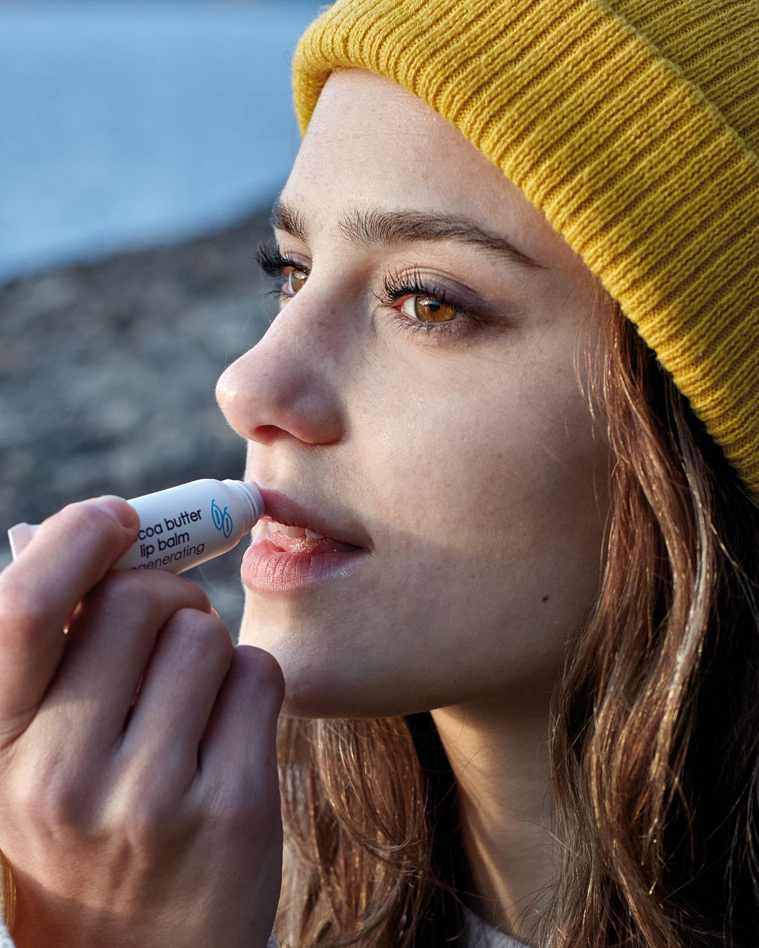 Person applying lip balm outdoors with a blurred background
