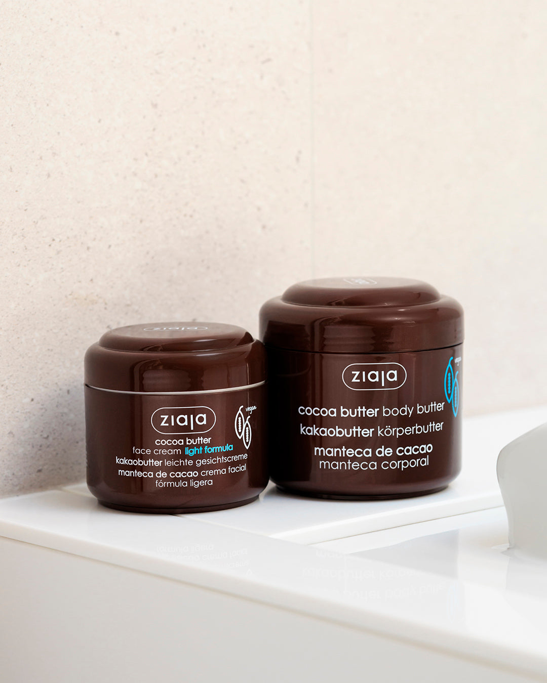 Two brown jars of Ziaja cocoa butter products, face cream light formula and body butter, placed on a white surface