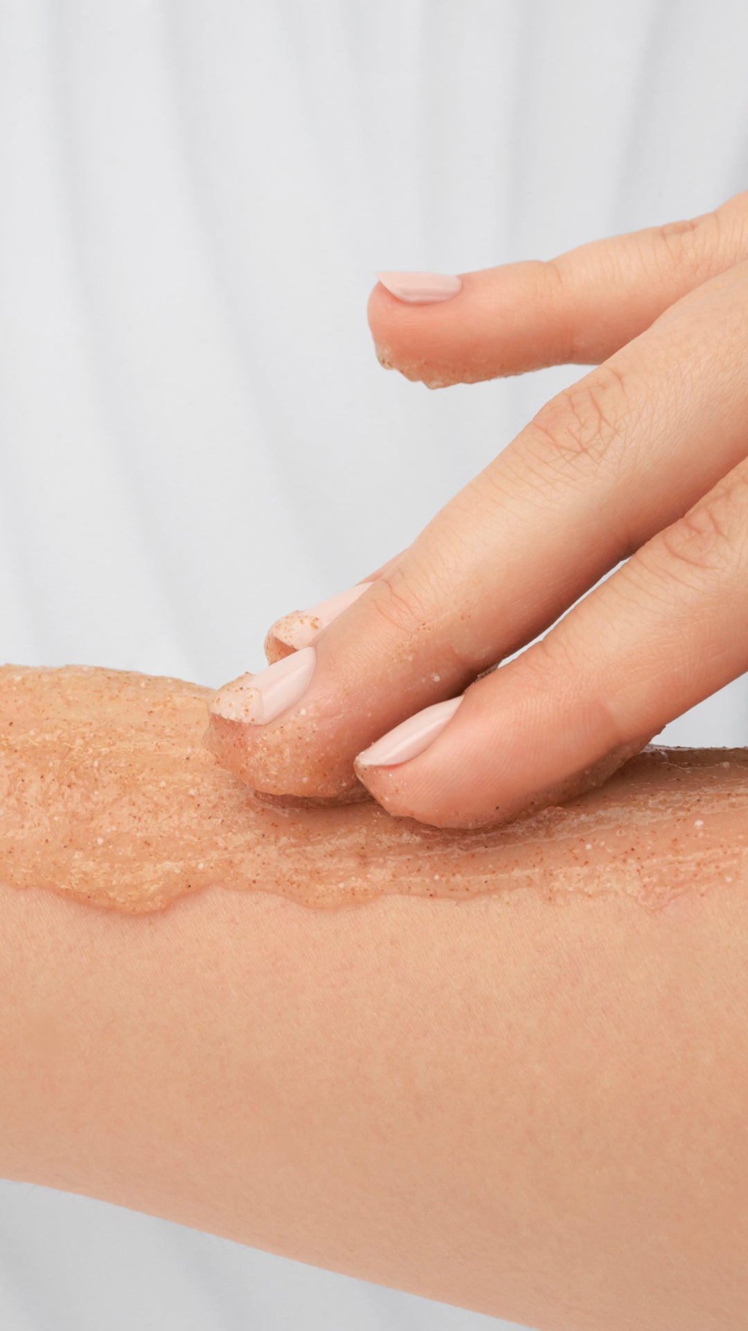 Hand applying a brownish Ziaja body scrub to a person's arm against a white background