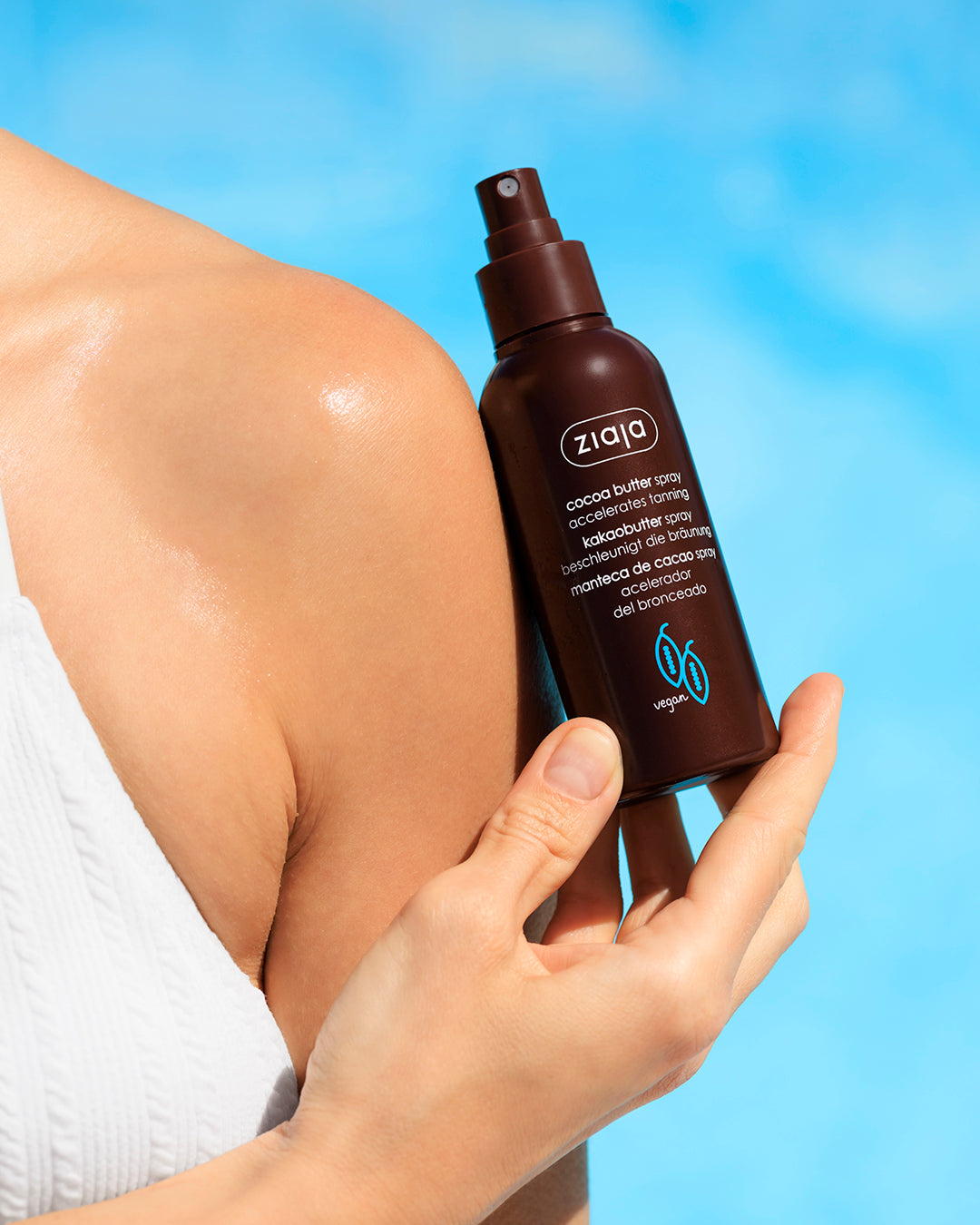 Hand holding a Ziaja cocoa butter spray against a blue sky background