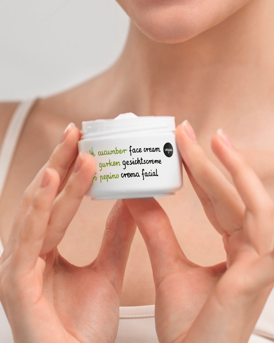 A close-up of a person holding a small white jar of Ziaja face cream with green and black text that reads 'cucumber face cream'.