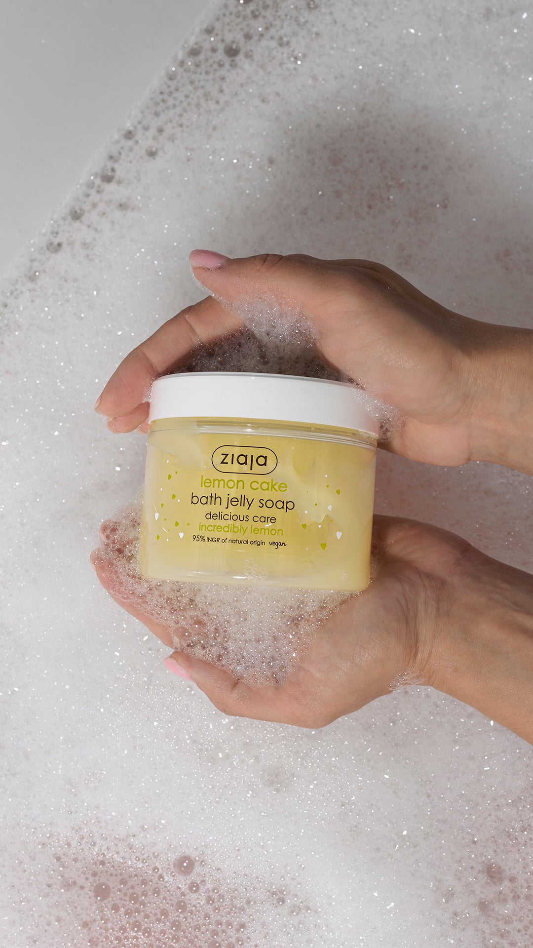 Hand holding a Ziaja product in a soapy water setting