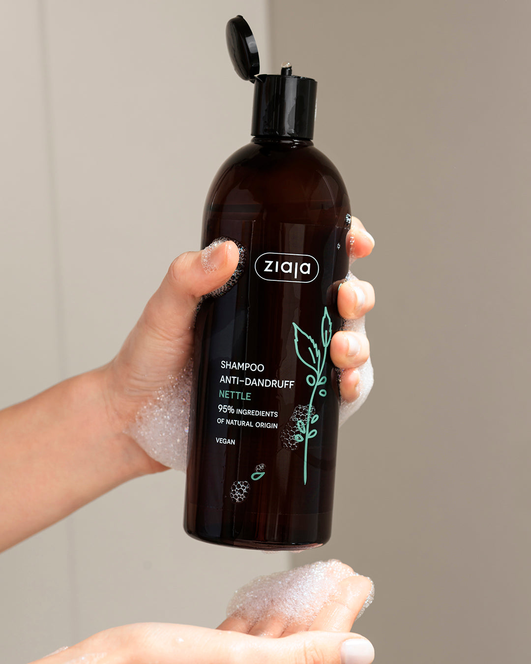 Ziaja nettle anti-dandruff shampoo in brown bottle, vegan formula with 95% natural origin ingredients, cleansing scalp care with foam in hands