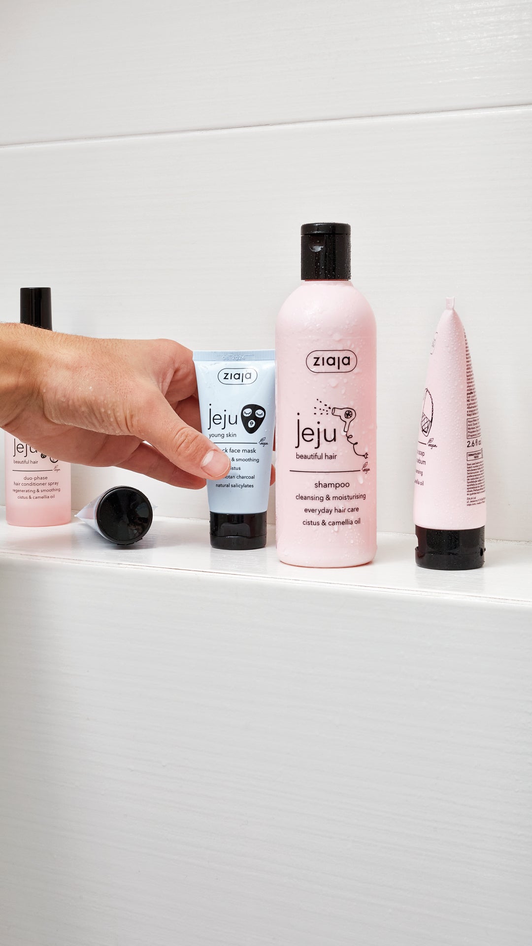 Hand reaching for a bottle of shampoo on a white shelf with various hair care products.
