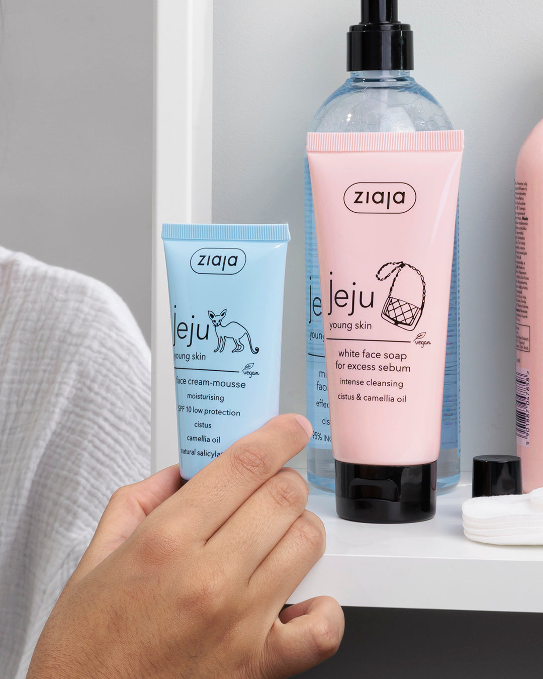 Hand holding a Ziaja skincare product with other skincare items in the background.