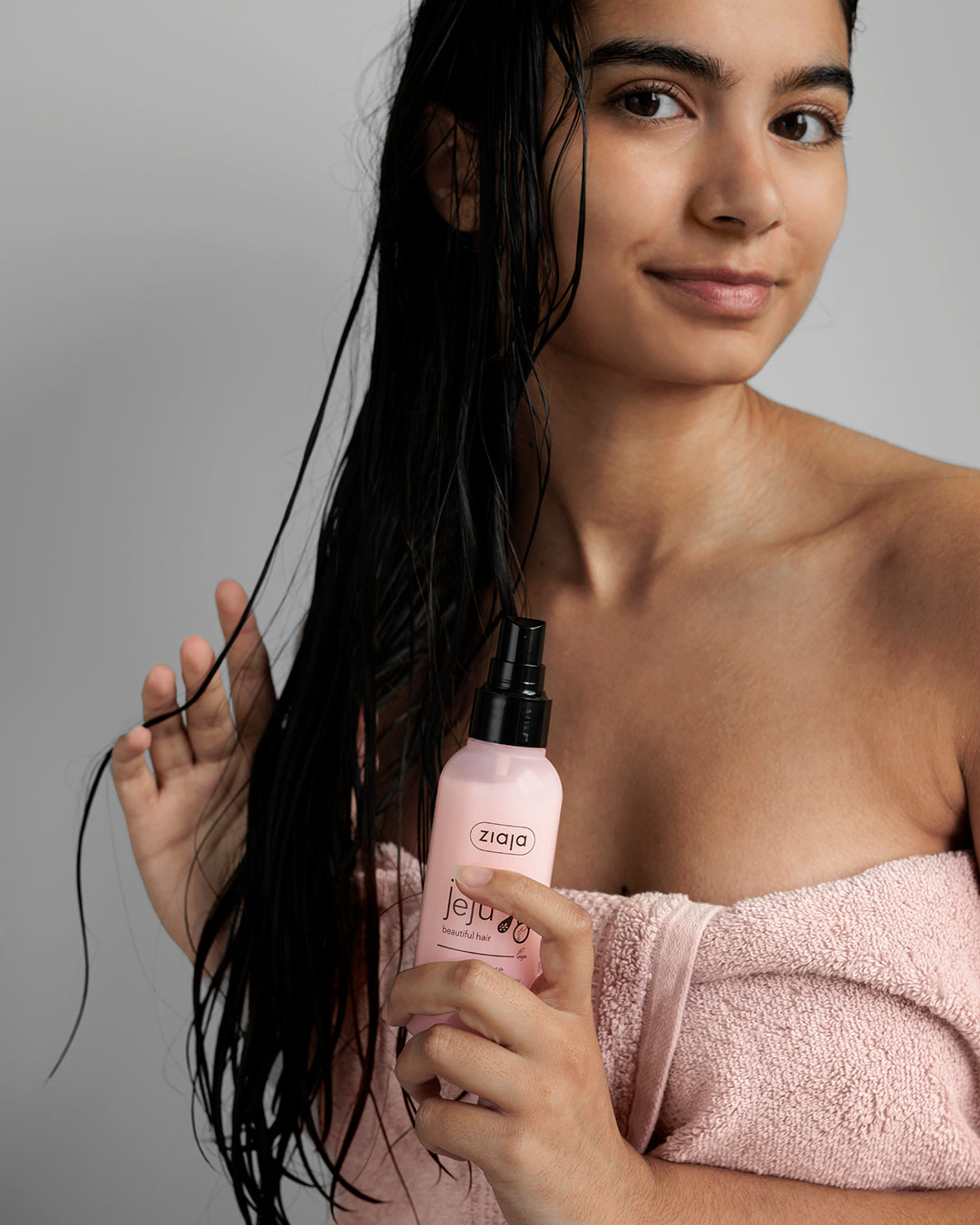 Woman holding a pink bottle labeled 'Ziaja' with wet hair against a gray background
