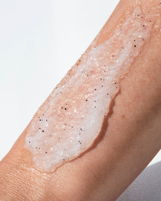 Close-up of a hand with a white body scrub with a black-speckled texture applied to the skin.