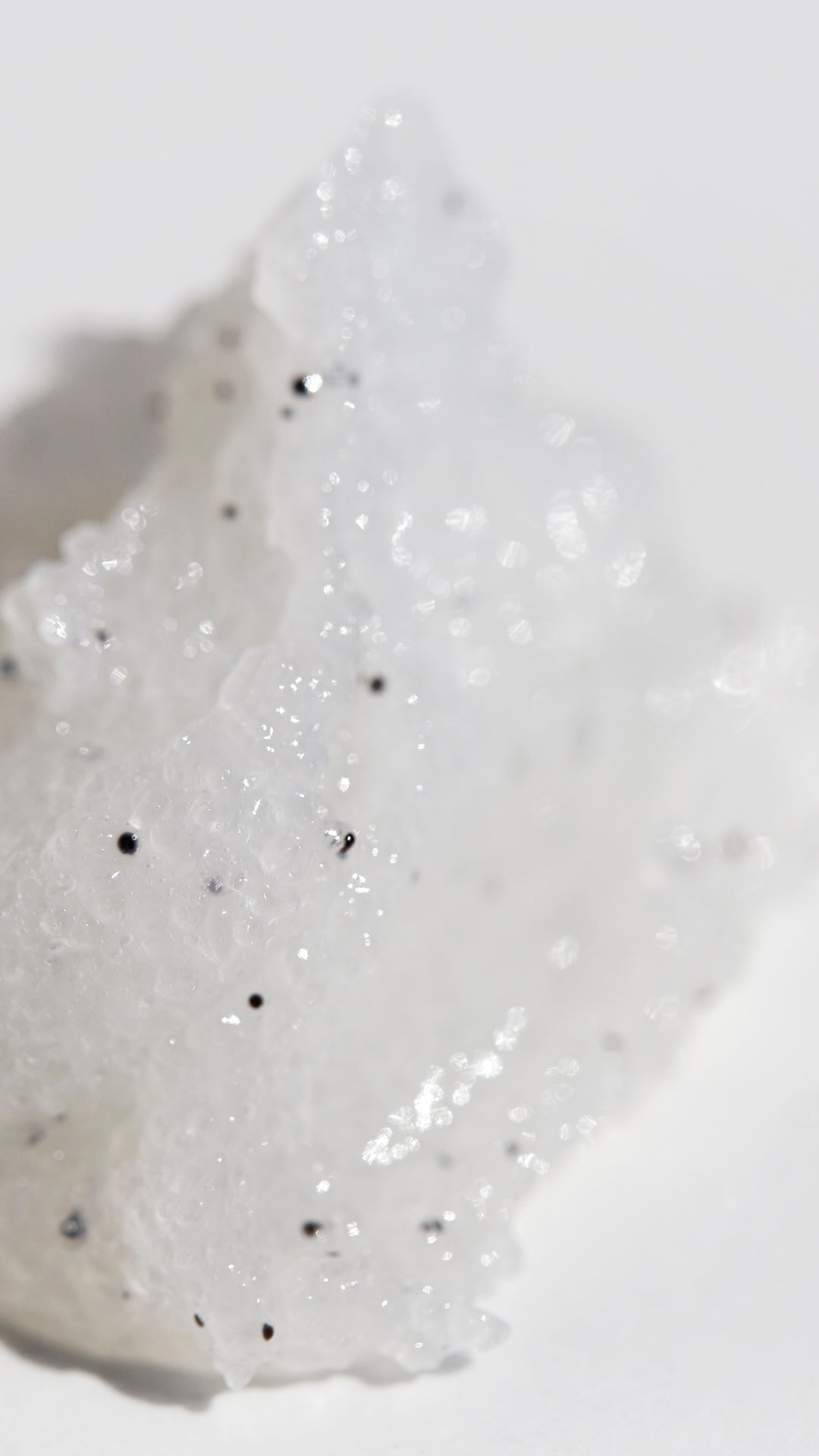 Close-up of a white body scrub  with black specks on a light gray background