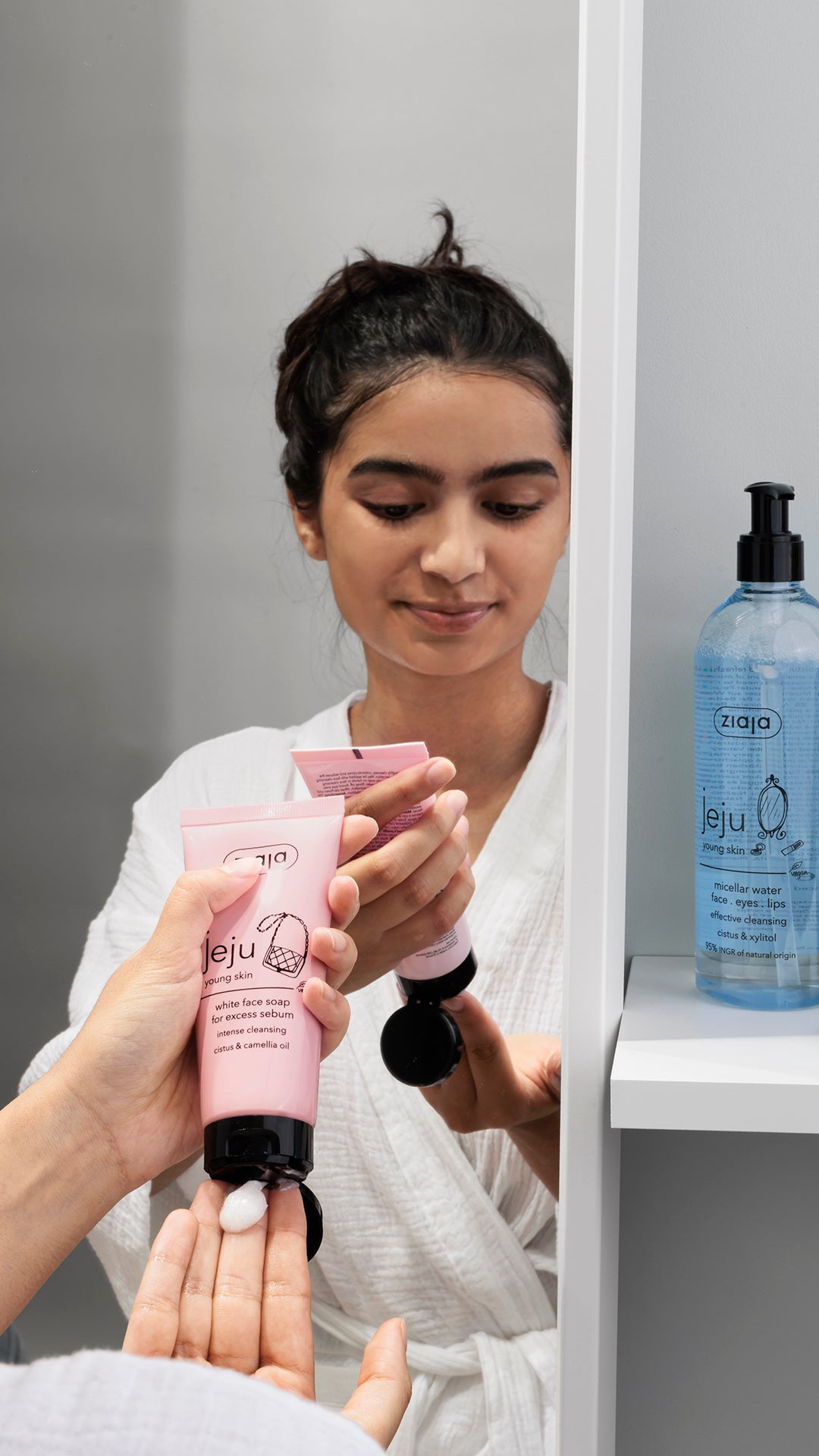 Woman in a bathroom holding pink skincare products with Jeju branding.