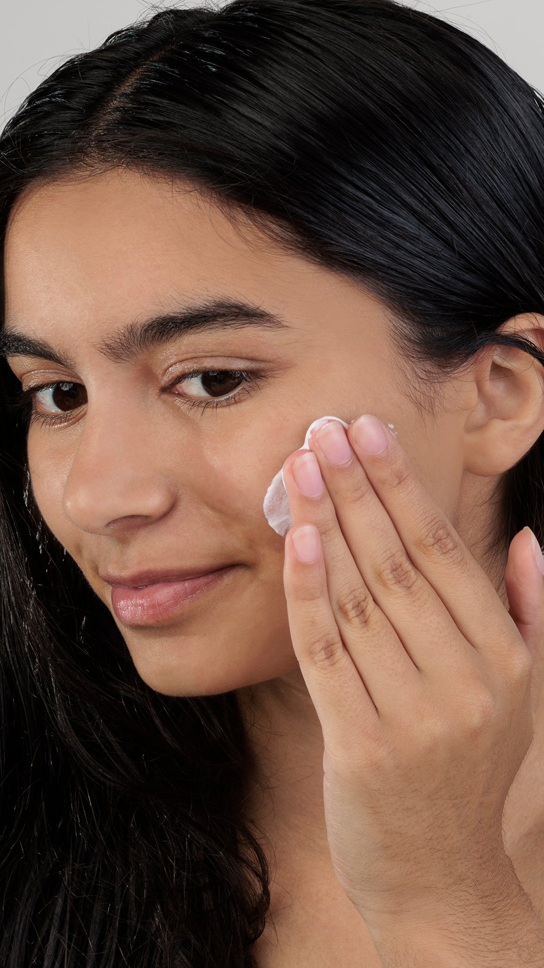 Woman applying cream to her face with a neutral background