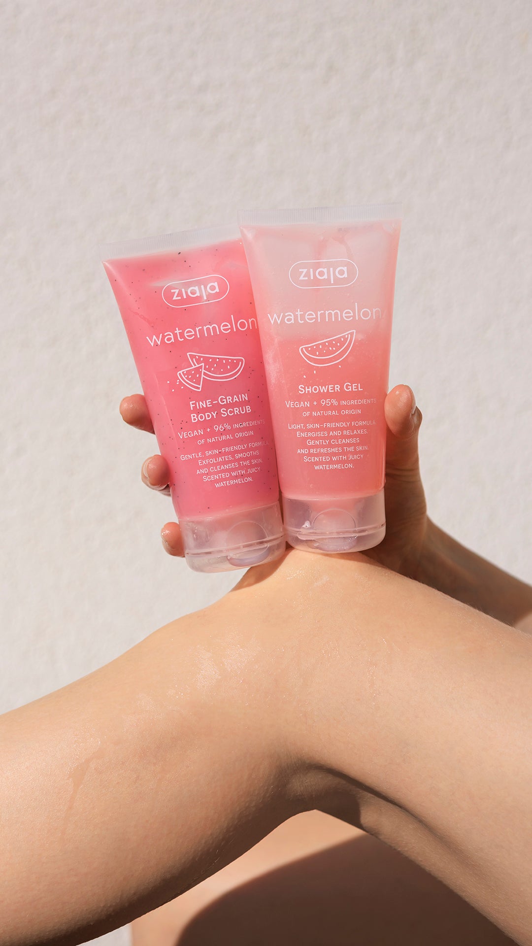 Two pink Ziaja watermelon body scrubs held by a person against a neutral background