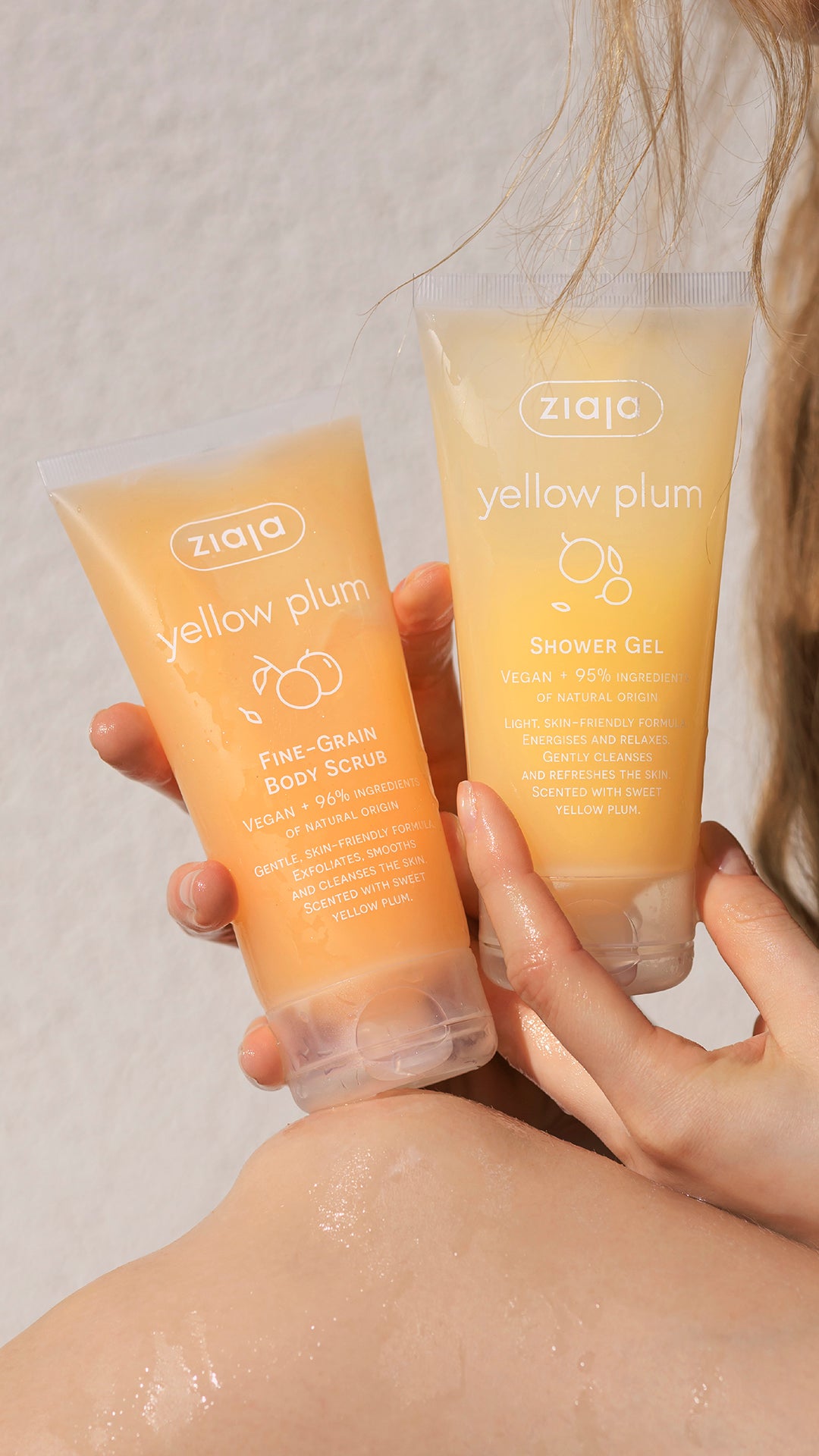 Two bottles of Ziaja Yellow Plum skincare products held by a person against a neutral background.