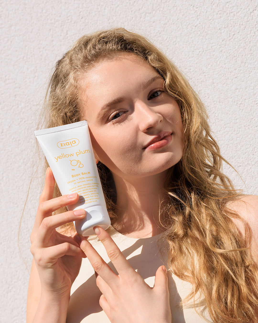 Woman holding a skincare product against a light background