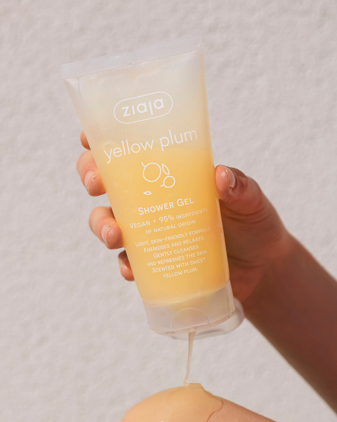 Hand holding a bottle of Ziaja Yellow Plum shower gel against a plain background
