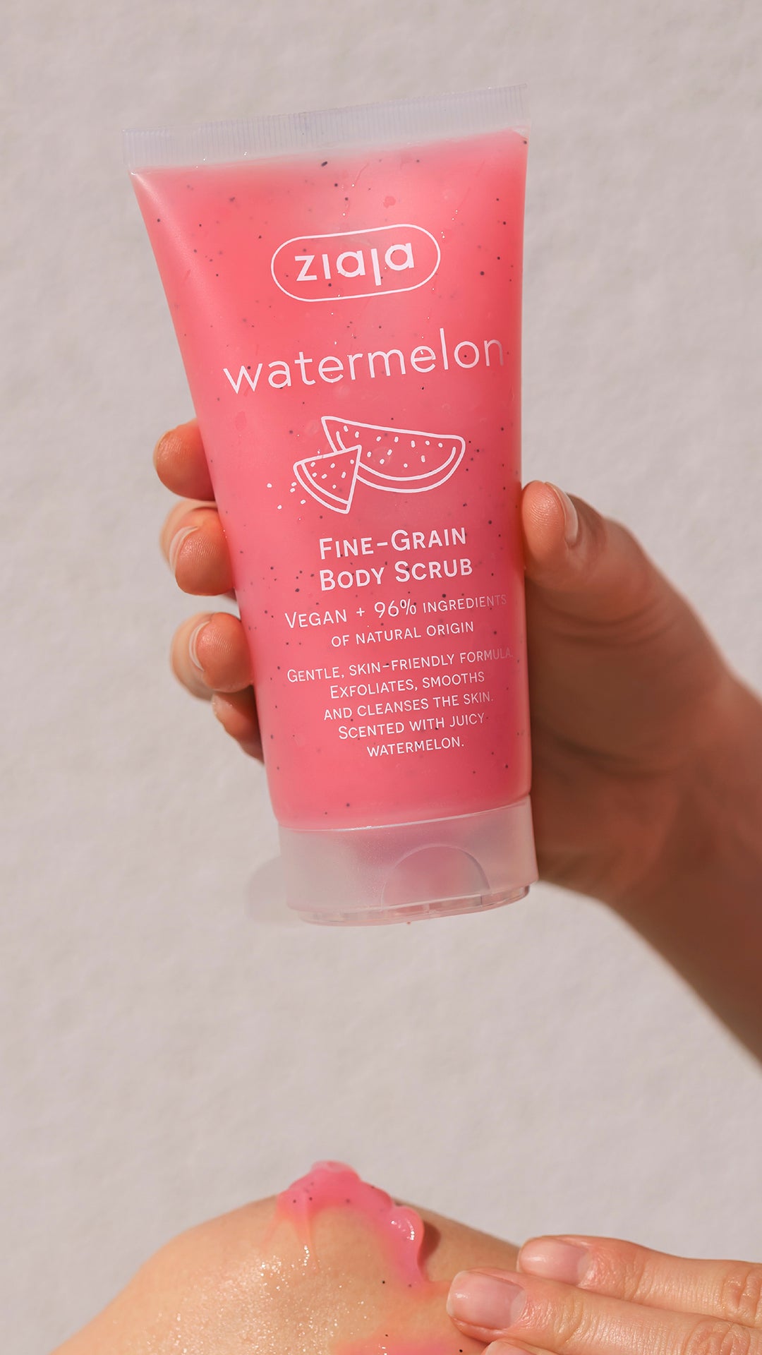 Hand holding a pink body scrub labeled 'watermelon' by Ziaja against a neutral background.