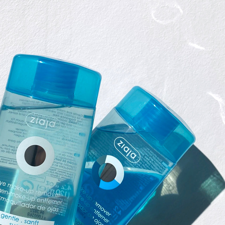 Ziaja Gentle Eye Make-Up Remover in two blue bottles on a white background, shown close-up with light reflections.