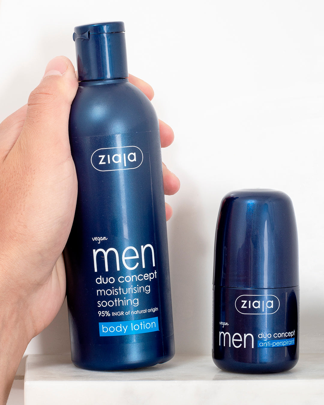 Hand holding Ziaja Men Duo Concept body lotion next to Ziaja Men Duo Concept anti-perspirant on a bathroom shelf.